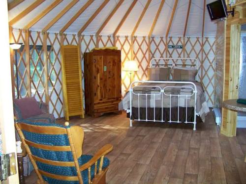Cozy yurt interior featuring a bed, wooden furniture, and warm lighting, with a rustic, inviting atmosphere.