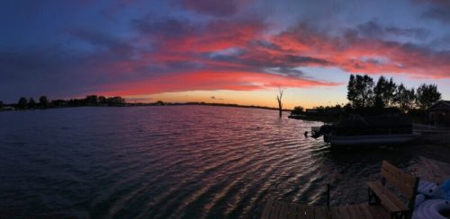 A serene lakeside view at sunset, featuring vibrant pink and orange skies reflecting on the water.