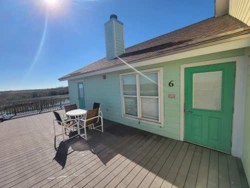 A sunny deck with a table and chairs, featuring a green door and light blue walls, overlooking a scenic view.