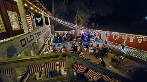 A lively outdoor gathering at night, with string lights, people socializing, and a festive atmosphere.