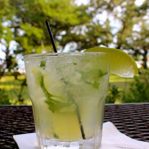A refreshing mojito in a glass with mint, lime, and a straw, set against a blurred outdoor background.