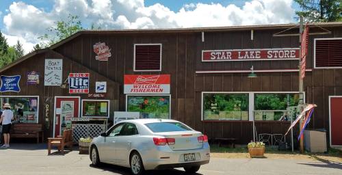 A rustic store with signs welcoming fishermen, surrounded by trees and a parked car in front.