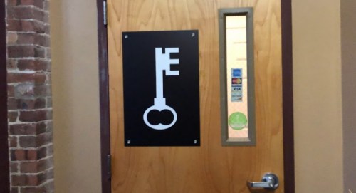 A wooden door with a key symbol on a black sign and a small window beside it.