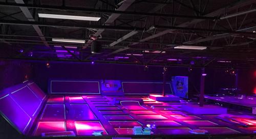 A dimly lit trampoline park with vibrant purple and pink lights illuminating the jumping areas.