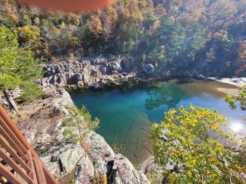 A scenic view of a clear blue-green pond surrounded by rocky cliffs and autumn foliage.