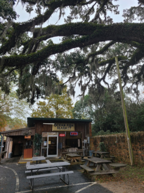 A rustic fish market with outdoor picnic tables, surrounded by trees draped in Spanish moss.