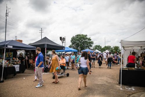 A bustling outdoor market with vendors, tents, and a crowd of people browsing and enjoying the event.