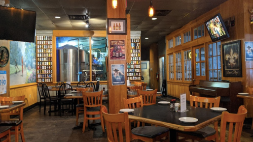 A cozy restaurant interior with wooden tables, chairs, and a bar area, featuring wall art and a large brewing tank.