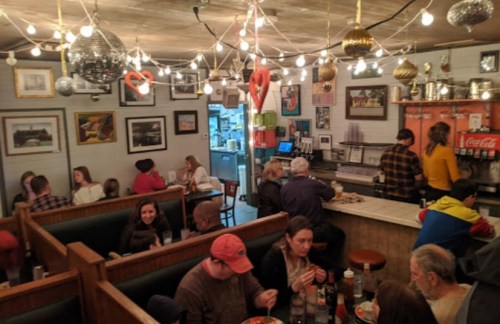 A cozy diner with patrons in booths, a bar area, and festive string lights overhead.