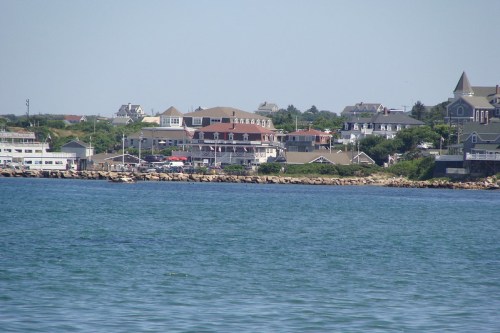 Coastal view of a shoreline with houses and a rocky beach under a clear blue sky.