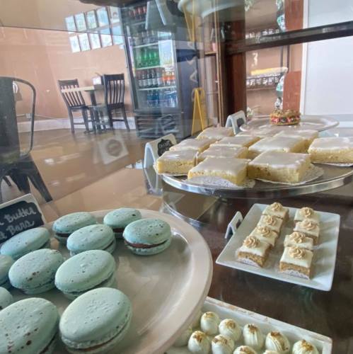 A display case filled with colorful macarons, lemon bars, and small desserts in a cozy café setting.