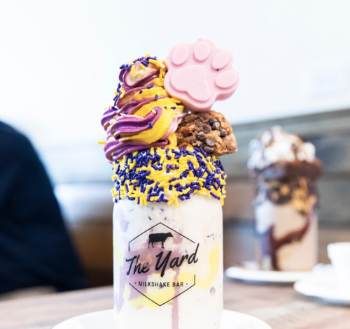 A colorful milkshake topped with whipped cream, sprinkles, and a pink paw-shaped candy in a branded glass.