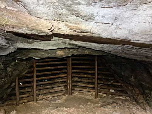 A dimly lit cave interior with a rocky ceiling and wooden slatted structure at the entrance.