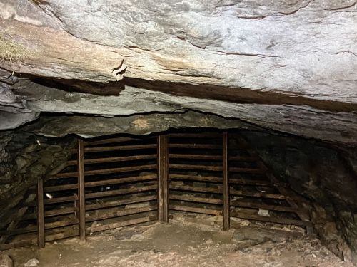 A dimly lit cave interior with a rocky ceiling and wooden slatted structure at the entrance.