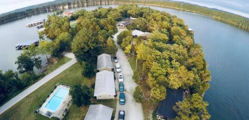Aerial view of a lakeside property with cabins, a pool, and a winding road surrounded by trees and water.