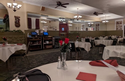 A cozy restaurant interior with white tablecloths, red roses on tables, and a warm, inviting atmosphere.