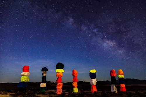 Colorful rock formations stand under a starry sky, with the Milky Way visible in the background.