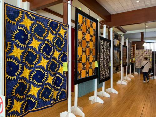 A display of colorful quilts hanging in a gallery, showcasing various patterns and designs.
