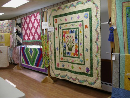 A display of colorful quilts hanging in a room, showcasing various patterns and designs.