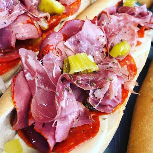 Close-up of a sub sandwich loaded with layers of salami, ham, and pickles on a soft hoagie roll.