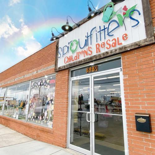 Exterior of Sproutfitters Children's Resale store, featuring a brick facade and a colorful sign, under a rainbow.