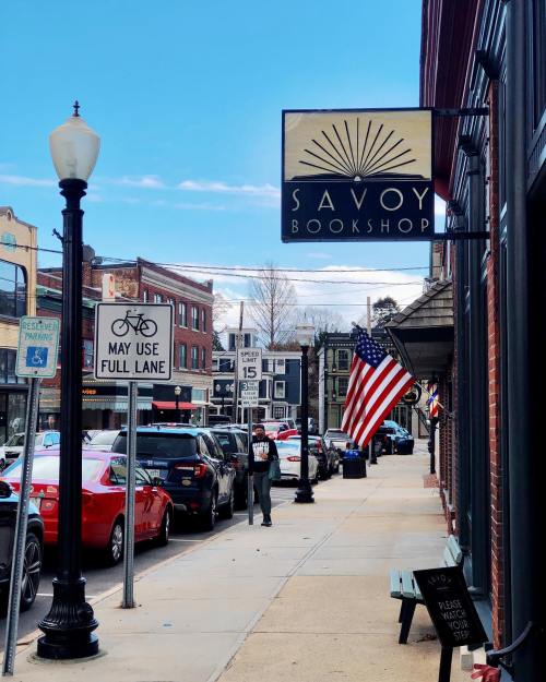 A street view of Savoy Bookshop with parked cars, an American flag, and a clear blue sky.