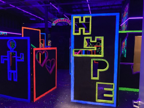 Colorful neon art installations with the word "HOPE" and various shapes in a dark, illuminated space.