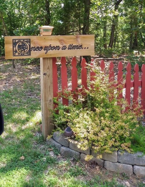 A wooden sign reading "Once upon a time..." next to a red fence and a small bush in a wooded area.