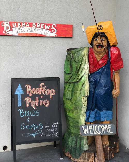 A wooden statue of a man holding a spear stands next to a sign for a rooftop patio with games and brews.