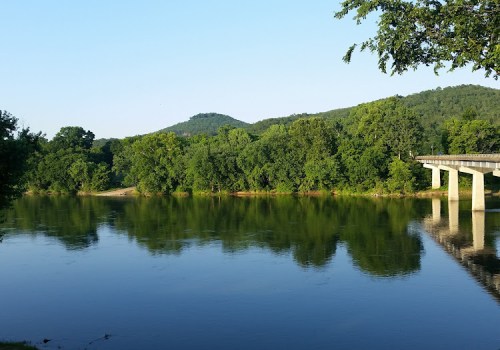A serene river scene with lush green trees and a bridge reflecting on the calm water under a clear blue sky.
