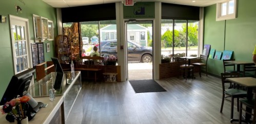 Interior of a shop with green walls, a counter, and artwork displayed. A view of the outside through the entrance.