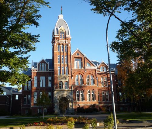 Historic brick building with a tall tower, surrounded by trees and clear blue sky.