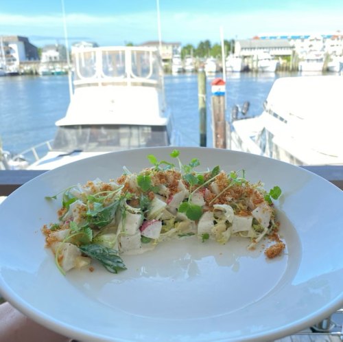 A fresh salad with greens and toppings, served on a plate with a marina view in the background.