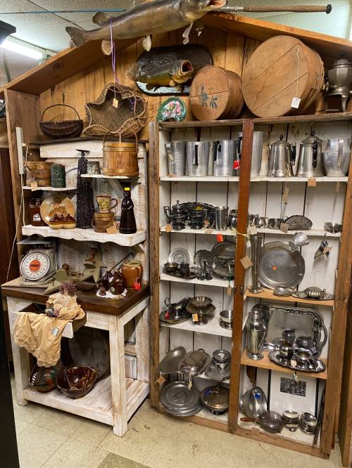 A display of various antique items, including glassware, metalware, and wooden objects, in a vintage shop setting.