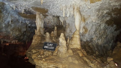 Stalactites and stalagmites in a cave, with a sign reading "Cliff Dwellers" in the foreground.