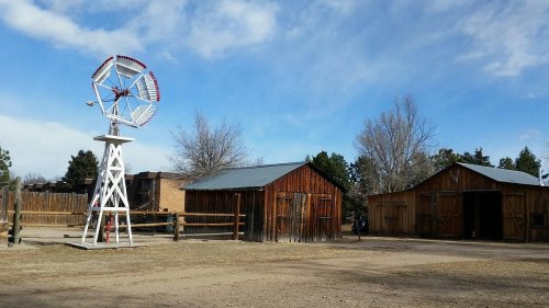 A rustic scene featuring a white windmill and two wooden barns under a blue sky with scattered clouds.
