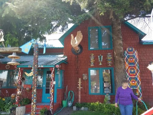 A colorful, quirky house with decorative elements, including a large hand sculpture and a woman in a purple sweater.