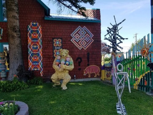 Colorful outdoor art installation featuring a bear sculpture holding children, surrounded by vibrant murals and decorations.