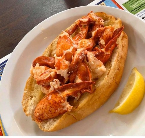 A lobster roll on a toasted bun, filled with chunks of lobster meat and served with a lemon wedge.