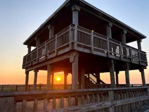 A wooden observation tower at sunset, with warm colors illuminating the sky and surrounding landscape.