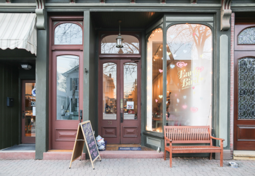A charming storefront with large windows, a bench outside, and a sign featuring hearts.
