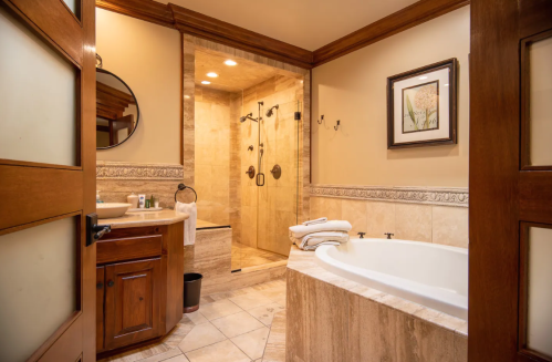 A luxurious bathroom featuring a soaking tub, walk-in shower, and wooden accents. Soft lighting enhances the serene atmosphere.