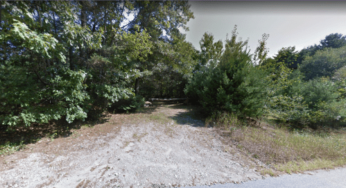 A gravel path leads into a wooded area with dense trees and shrubs on either side.