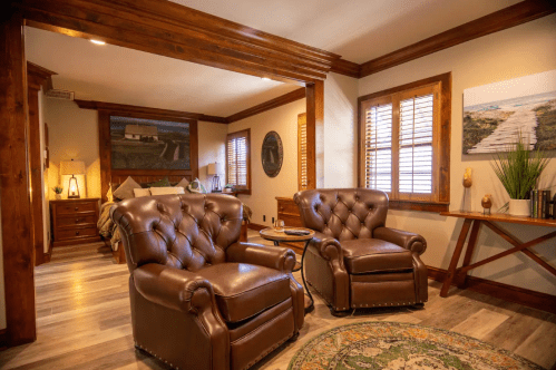 Cozy room featuring two brown leather chairs, a wooden table, and a bed in a warm, inviting atmosphere.