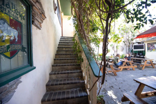 A stone staircase leads up from a courtyard with picnic tables and greenery, framed by a building's wall.