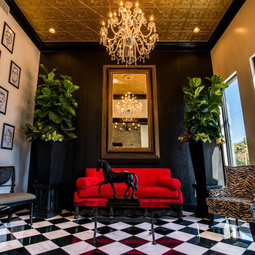 A stylish interior featuring a red sofa, black horse statue, large mirror, and elegant chandelier against a checkered floor.
