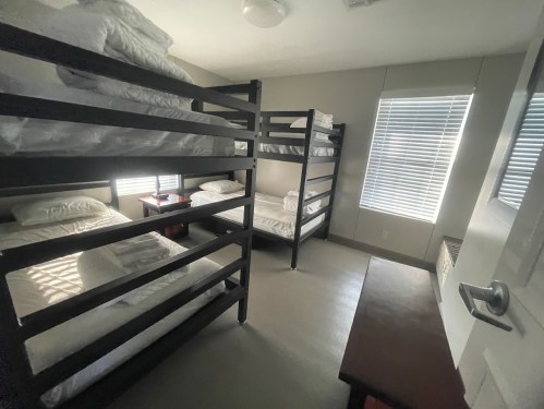 A simple room with two sets of bunk beds, a small table, and natural light from windows.
