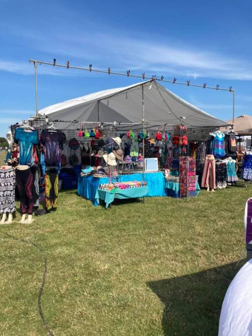 A vibrant market stall with colorful clothing and accessories under a tent on a sunny day.