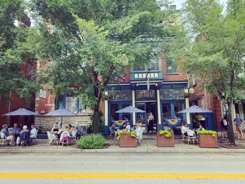 A vibrant street scene with a restaurant featuring outdoor seating, colorful umbrellas, and rainbow decorations.