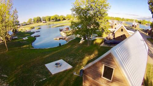 A scenic view of a lakeside area with cabins, trees, and a calm waterway under a clear blue sky.